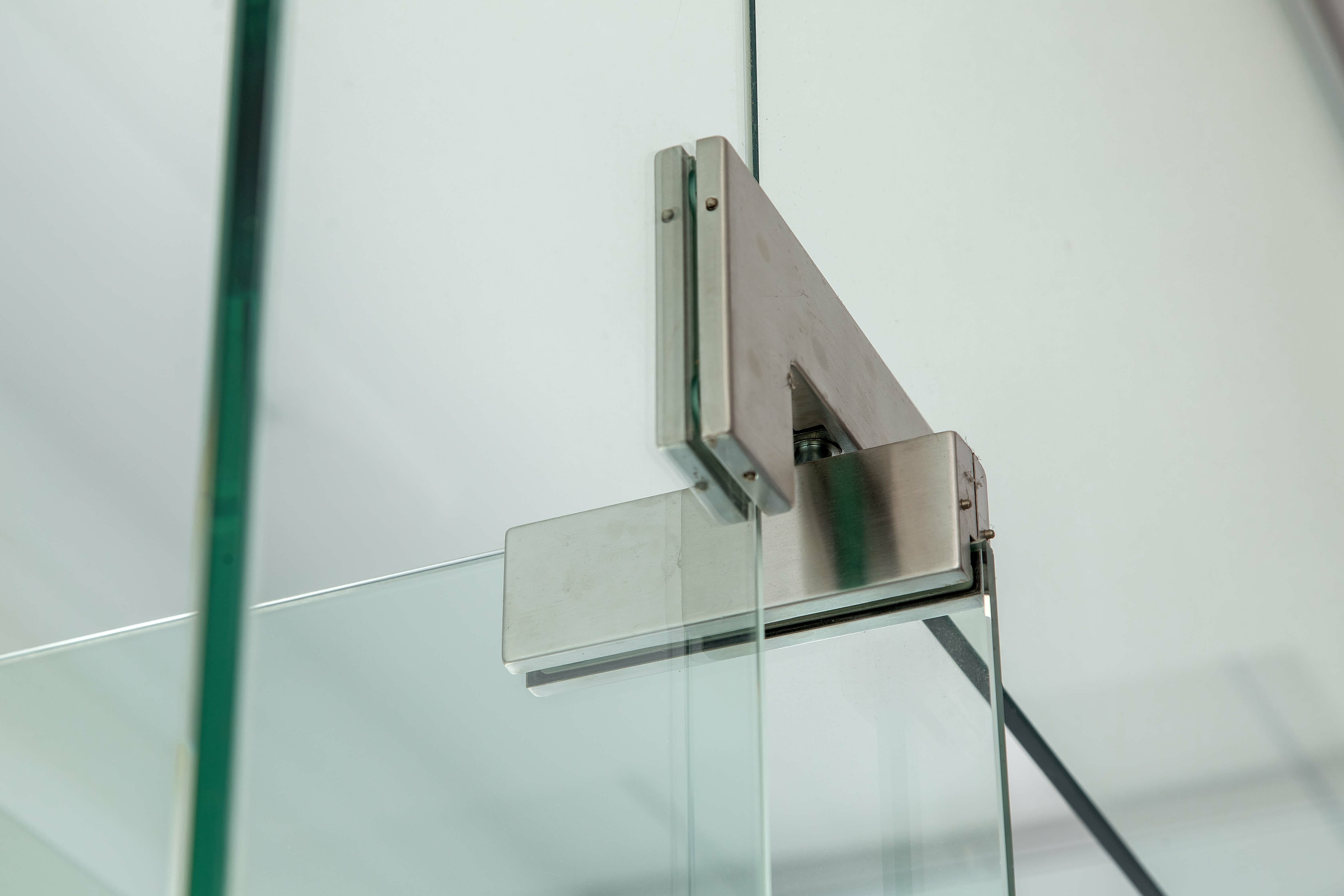 Close-up of a brushed metal patch fitting mounted on the corner of a clear glass door.